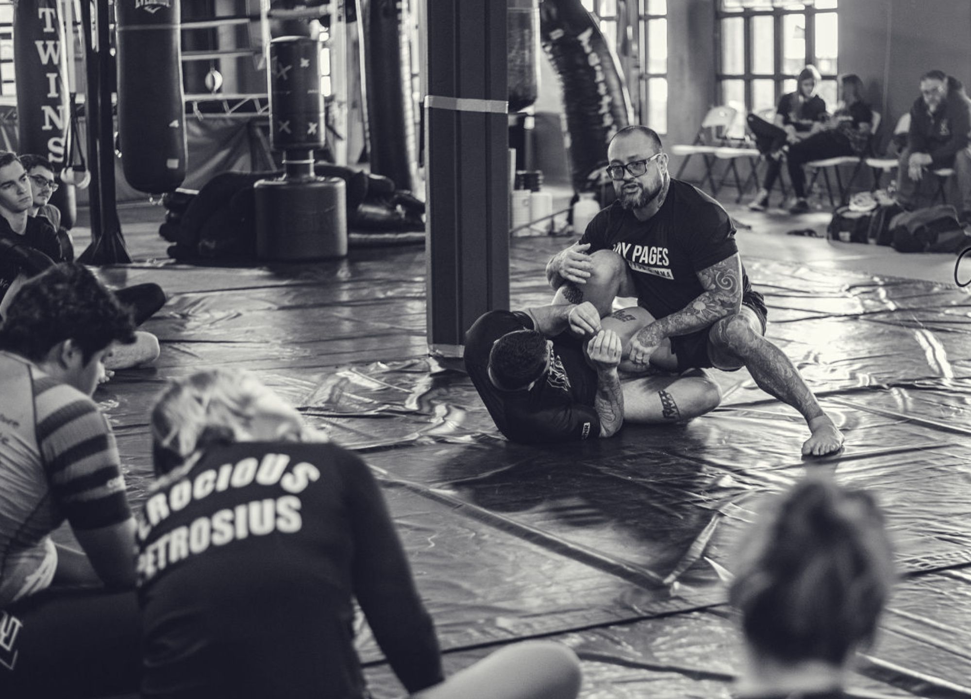 Adult striking drill at KRM: a coach corrects form while a partner holds pads on the training mats.